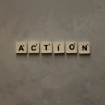 Scrabble tiles forming the word 'Action' on a textured gray surface, conveying motivation.
