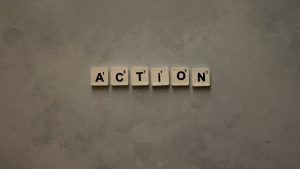 Scrabble tiles forming the word 'Action' on a textured gray surface, conveying motivation.