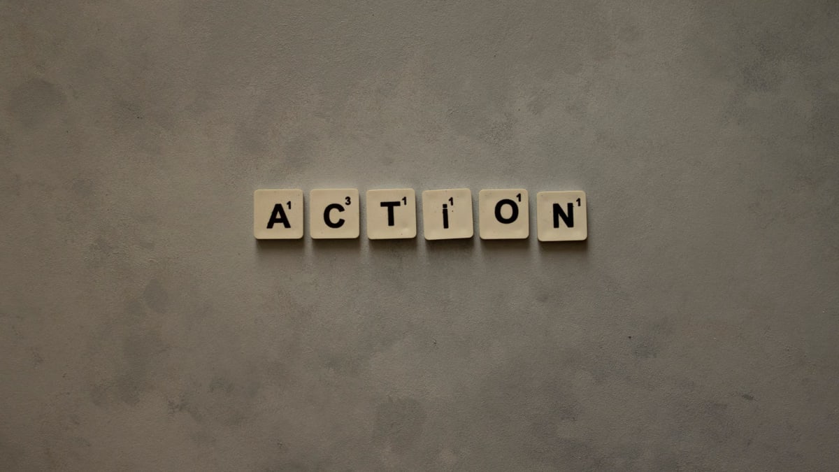 Scrabble tiles forming the word 'Action' on a textured gray surface, conveying motivation.